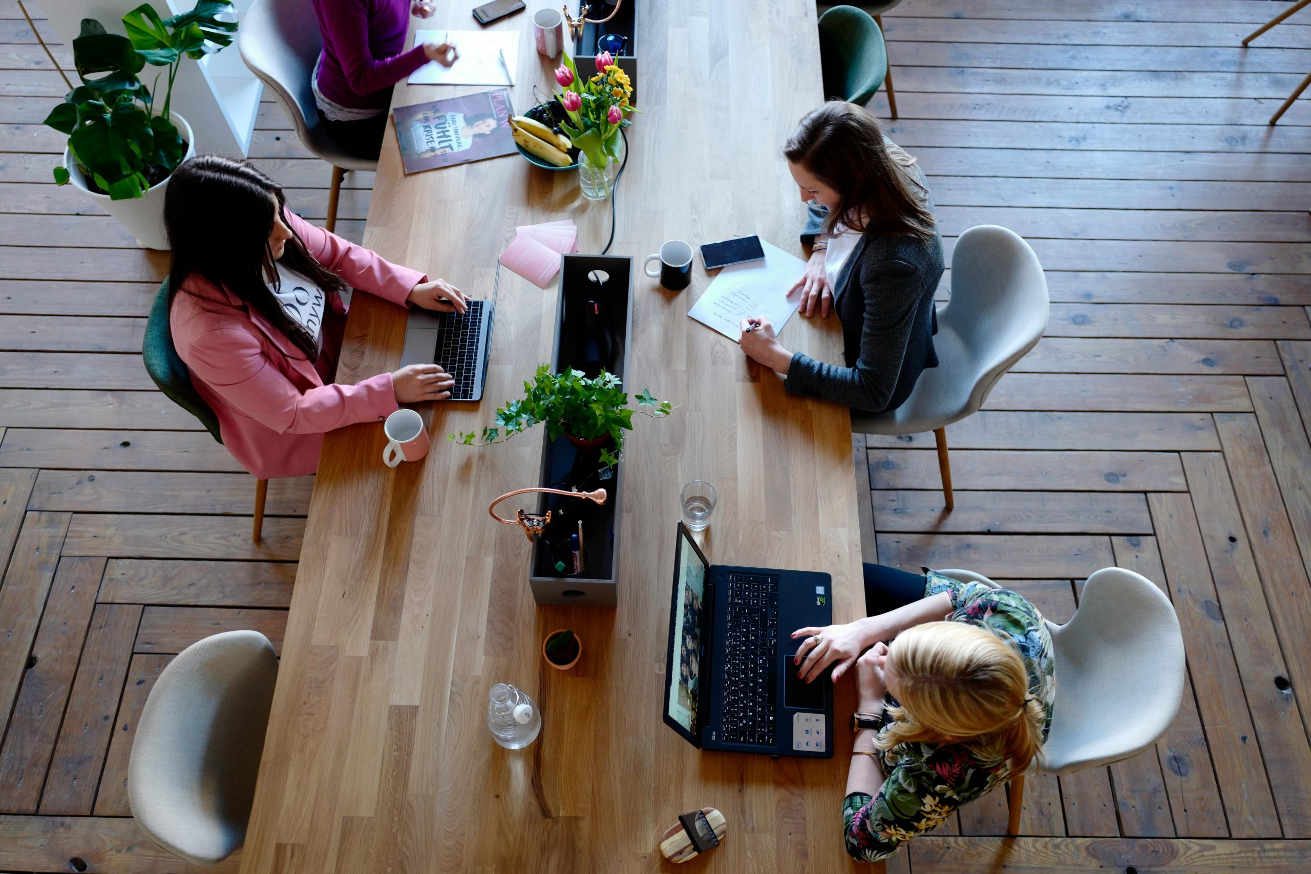 Tres mujeres sentadas en sillas blancas frente a una mesa, participando en una reunión.